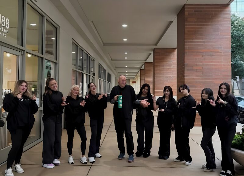 Todd Faulk standing outside with a group of cosmetology students in matching black apparel under the walkway at Aveda Arts Dallas.