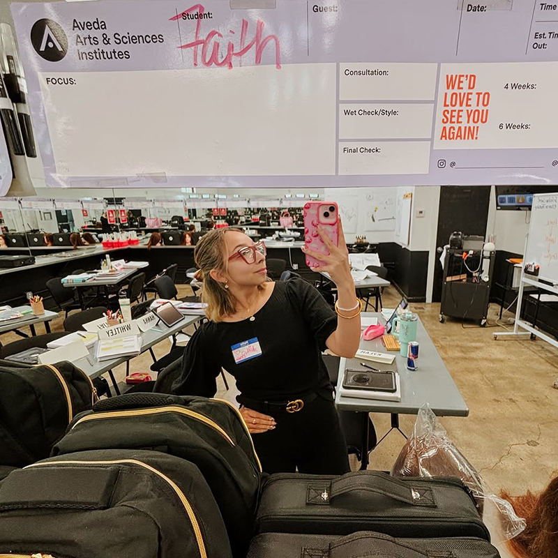 Beauty school student taking selfie picture in mirror on campus at Aveda Arts.