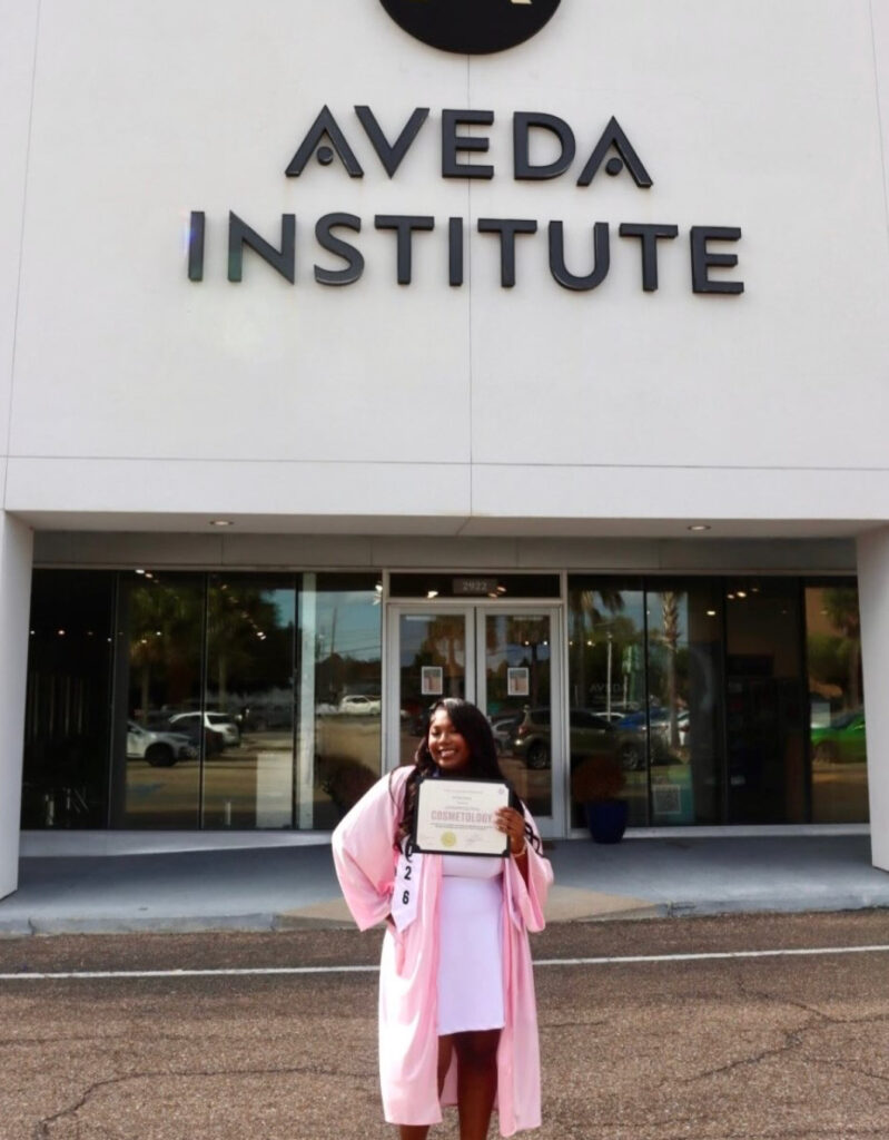 Aveda Arts graduating cosmetology student in front of the Institute holding a diploma